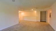 This two-floor space offers a functional and straightforward layout designed to maximize usable area. The main living space is finished with wall-to-wall carpeting in a neutral tone, creating a warm and cohesive feel throughout. A notable architectural feature is the curved partial dividing wall, which subtly separates areas within the open floor plan while maintaining a sense of spaciousness and flow between zones.

Track lighting is mounted on the ceiling, providing adjustable and practical illumination across the room. The neutral, light-toned walls contribute to a bright and airy ambiance, even in interior-facing areas. A built-in shelving unit is positioned along one wall, offering convenient storage or display space without the need for additional furniture.

Doorways lead to connected rooms and additional areas, suggesting a well-connected floor plan that facilitates easy movement throughout the space. The overall design is clean and understated, with an emphasis on open space and utility. The second floor adds further versatility to the layout, accommodating a variety of uses across the two levels. This space presents a blank canvas well-suited to a range of configurations and purposes.