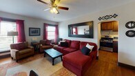 Located at 304 W Touhy Ave in Park Ridge, Illinois, this single-floor residence offers a thoughtfully arranged layout that maximizes comfort and functionality throughout. The living room serves as the heart of the space, anchored by a generous sectional sofa and complemented by a classic ceiling fan overhead. Natural light filters in through windows dressed with bold red curtains, while a large dark-framed wall mirror adds depth and visual interest. A cast-iron radiator adds a touch of vintage character to the room. The kitchen features rich dark wood cabinetry, light granite-style countertops, hardwood flooring, and stainless steel appliances, providing a practical and attractive cooking environment. The bedroom is a calm retreat, offering hardwood floors, multiple windows with blinds and neutral drape panels that allow for ample natural light, a dresser, and tasteful wall décor including framed artwork and display shelves. The bathroom is clean and straightforward, with white tile flooring, a white vanity, and a shower-tub combination behind a white curtain, framed by dark door trim. Overall, the space presents a warm, lived-in ambiance with a cohesive blend of classic and contemporary elements.