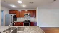 Located at 7040 Gentle Shade Rd in Columbia, Maryland, this single-floor residence offers a thoughtfully designed open-concept layout that connects the kitchen, dining, and living areas seamlessly. The kitchen serves as a central highlight, featuring rich cherry wood cabinetry, granite countertops, a subway tile backsplash, and a full suite of stainless steel appliances including a range, over-the-range microwave, and refrigerator. A peninsula with a built-in sink and pendant lighting above adds both function and visual appeal, creating a natural division between the kitchen and the adjoining living space.

The living area transitions between warm hardwood-style flooring and plush carpeting, offering a comfortable and versatile environment. Track lighting in the main living zone provides adjustable illumination, while a sliding glass door allows natural light to enter and provides outdoor access. Built-in shelving adds a practical storage element to the space.

The bedroom is generously proportioned, featuring soft carpet, a ceiling fan, a window with natural light, and a closet with built-in shelving. The bathroom is finished with tile flooring, a granite-topped cherry vanity, and a full tub-shower combination with clean white tile surround.