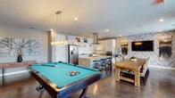 Located at 2000 Front St in Summerville, SC, this single-floor community space offers a thoughtfully designed, open-concept layout that seamlessly blends entertainment, dining, and relaxation. Polished concrete floors run throughout, lending the space an urban, contemporary feel that ties each zone together cohesively.

The fully equipped kitchen is a standout feature, showcasing white shaker cabinetry, granite countertops, stainless steel appliances including a French door refrigerator, wall oven, microwave, and dishwasher. A large central island with bar seating provides an ideal gathering spot, while a striking herringbone tile accent wall and glass pendant hood add visual interest. Track lighting illuminates the workspace efficiently.

Adjacent to the kitchen, a spacious dining area accommodates a large farmhouse-style table with ample seating. The entertainment zone centers around a full-size billiards table beneath modern rectangular pendant lighting, creating a lively focal point for social gatherings.

The lounge area transitions into a more relaxed setting, featuring sectional and dual-sofa seating arrangements, a patterned area rug, a gold drum coffee table, and a wall-mounted flat-screen TV flanked by decorative sconce lighting. Curated artwork and neutral tones throughout contribute to a polished, welcoming ambiance well-suited for community events and casual socializing.