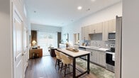 This well-appointed 2-bedroom, 3-bathroom single-floor residence offers a thoughtfully designed open-concept layout that maximizes both functionality and style. The kitchen is a standout feature, outfitted with light wood cabinetry, grey subway tile backsplash, stainless steel appliances including a side-by-side refrigerator, electric range, built-in microwave, and dishwasher, all complemented by white quartz countertops. A kitchen island with bar seating provides additional prep and dining space. The kitchen flows seamlessly into the living room, which features wood-style flooring, elevated ceilings, and a large sliding glass door that floods the space with natural light and opens to an outdoor area. The primary bedroom offers a comfortable retreat with plush carpet, a bold accent wall, and a dedicated walk-in closet with built-in shelving and hanging storage. The second bedroom also features carpet flooring, vaulted ceilings, and a bright window with outdoor views. Each of the three bathrooms is finished with wood-tone vanities, white countertops, and tub-shower combinations with clean tile surrounds. A utility room and additional closet round out the functional layout of this modern, move-in-ready residence.