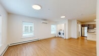 Located at 8 Admiral Harry Rich Dr in Brunswick, Maine, this thoughtfully designed one-bedroom, one-bathroom residence offers a clean, modern aesthetic throughout its single floor. Light hardwood flooring runs through the main living areas, complementing the bright white walls and flush circular ceiling fixtures that keep the space feeling open and airy.

The open-concept kitchen and living room serves as the heart of the home. The kitchen features rich, dark taupe cabinetry with ample upper and lower storage, stainless steel appliances including a refrigerator and range, a white quartz peninsula countertop with an undermount sink, and a dishwasher. The living area is generously proportioned, bathed in natural light from multiple windows with blinds, and is equipped with a wall-mounted mini-split for climate control as well as baseboard heating. A dedicated in-unit laundry area with a full-size washer and dryer adds everyday convenience.

The bedroom is a comfortable, quiet retreat finished with soft carpet and subtle blue-gray walls. A double-door closet provides solid storage, and a window offers natural light and exterior views. The full bathroom is ADA-accessible, featuring stainless grab bars, a floating vanity with white countertop, a large mirror, and hardwood-style flooring with a natural light-filled window.