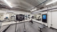 Located at 127 N Elizabeth St in Lima, Ohio, this fitness center offers a comprehensive, single-level workout facility designed to support a wide range of exercise routines. The space features an industrial aesthetic, with exposed concrete ceilings, visible ductwork, and structural columns that lend the facility a raw, utilitarian character. Durable rubber flooring spans the entirety of the space, providing a safe and functional surface for all types of physical activity.

The cardio area is well-stocked with multiple treadmills and a stationary cycling bike, several of which are equipped with integrated display screens for interactive workout experiences. Large wall-mounted mirrors run along key sections of the space, visually expanding the facility and allowing users to monitor their form during exercise. Wall-mounted flat-screen televisions provide additional entertainment options.

The strength training zone includes a cable machine, an adjustable weight bench, and a multi-tiered dumbbell rack offering a range of free weights. A dedicated stretch and functional fitness area features stability balls, resistance accessories, and open floor space for bodyweight exercises. Split wall-mounted air conditioning units ensure climate control throughout the facility, and recessed and linear LED lighting provides consistent illumination across all areas of the space.