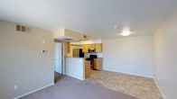 This single-floor space features an open-concept design that connects the living area and kitchen, creating a functional and cohesive layout. The living area is finished with plush carpeting, offering a comfortable feel underfoot, while the kitchen transitions to tile flooring, providing a practical and easy-to-clean surface. Neutral-toned walls throughout the space contribute to a bright and welcoming ambiance.

The kitchen is equipped with stainless steel appliances, including a refrigerator, microwave, and range, complemented by warm-toned wood cabinetry that adds a touch of warmth to the space. A peninsula-style counter separates the kitchen from the living area, offering additional workspace and serving as a casual dining or entertaining surface. Overhead cabinetry provides ample storage, keeping the space organized and efficient.

The layout also includes a doorway leading to additional areas of the unit, suggesting further functional spaces beyond the main living zone. A thermostat is conveniently mounted near the entryway, allowing for easy climate control. Flush-mount ceiling lighting ensures consistent illumination throughout, complementing the natural and artificial light sources in the space.