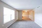 This single-floor residence offers a straightforward and functional layout across several well-defined areas. The living room is generously sized, featuring neutral-toned walls, soft wall-to-wall carpeting, and a large window dressed with vertical blinds that allows natural light to filter in. A front entry door is positioned conveniently off the living area, which opens further into a connected dining or secondary living space equipped with a ceiling fan and light fixture overhead.

The galley-style kitchen is efficiently organized with white cabinetry lining both sides, offering ample storage space. Light marble-patterned countertops run the length of the kitchen, complemented by a stainless steel sink, electric range, and white refrigerator. Light tile flooring and a window above the counter add brightness to the space.

The bedrooms are carpeted and feature neutral taupe-toned walls, ceiling fans with lighting, and windows that bring in natural light. One bedroom notably includes dual bi-fold closet doors, providing generous storage capacity, along with an additional doorway leading to further space.

The bathroom features a marble-style vanity countertop, an undermount sink, and a large mirror above. Clean white cabinetry beneath the vanity completes the space. Throughout the residence, consistent neutral tones and practical finishes create a cohesive and move-in-ready environment.