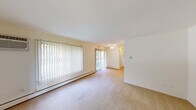 This 1-bedroom, 1-bathroom unit offers a practical and efficiently designed single-floor layout. The living room is the largest and most prominent space, featuring wall-to-wall carpeting, vertical blinds, a sliding glass door that brings in natural light and outdoor views of lush greenery, and a wall-mounted air conditioning unit alongside baseboard heating for year-round climate control. A ceiling fan adds additional comfort to the living area.

The bedroom is a comfortably sized private retreat, also carpeted, with a large window framing tranquil views of surrounding trees and baseboard heating. Adjacent to the bedroom is a dedicated closet for convenient storage.

The kitchen is appointed with white cabinetry, white countertops, a sink, and a full-size refrigerator, with warm hardwood-style flooring tying the space together in a clean and functional manner.

The bathroom features a full tub-shower combination with white tile surround, a toilet, a vanity with sink, a large mirror, and a Hollywood-style light bar above, creating a bright and practical space.

Throughout, the unit maintains a neutral, light color palette with cream-toned walls that contribute to a clean and airy atmosphere.