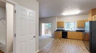 Located at 675 White Oak Cir in Independence, Oregon, this single-floor, 2-bedroom, 2-bathroom home offers a practical and comfortable layout designed for everyday living. The combined kitchen and living room serves as the heart of the home, with the kitchen featuring light wood cabinetry, dark granite-style countertops, wood-look vinyl flooring, and a full suite of black appliances including a refrigerator, range, microwave, and dishwasher. A window above the sink provides natural light throughout the space. The living room extends from the kitchen and opens directly to a private outdoor deck through sliding glass doors, offering pleasant views of surrounding greenery. Both bedrooms are carpeted in neutral tones with warm beige walls, offering a calm and comfortable atmosphere. The primary bedroom includes a sliding-door closet and a window overlooking the exterior. The second bedroom also features carpeted flooring, a window with outdoor views, and built-in wall heating. The two bathrooms are finished with wood-look vinyl flooring, warm wood vanity cabinetry, and dark countertops. One bathroom includes a walk-in shower with sliding glass doors, while the other features a full soaking tub. A hallway connects all rooms and conveniently houses an in-unit washer and dryer, adding to the home's functional appeal.