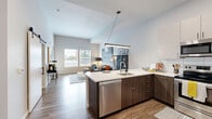 Located at 150 Main St in downtown Longmont, Colorado, this one-bedroom, three-bathroom residence offers a well-designed single-floor layout that maximizes every square foot. The open-concept living and kitchen area serves as the heart of the home, featuring soaring ceilings that amplify the sense of space and large windows that flood the room with natural light and offer views of the surrounding urban streetscape. The kitchen is outfitted with stainless steel appliances, a subway tile backsplash, two-tone cabinetry with crisp white uppers and warm wood-grain lowers, white quartz countertops, and a peninsula with bar seating — ideal for casual dining. Wood-look plank flooring flows throughout the main living areas, adding warmth and continuity. The bedroom is a comfortable retreat with plush carpeting, multiple windows, and generous wall space. A dedicated closet area and in-unit laundry add practical convenience. The bathrooms reflect a clean, modern aesthetic, with wood-grain vanities, large mirrors, and tile surround tub-shower combinations. An outdoor patio provides direct access to the streetside environment. The overall design balances contemporary style with functional living in the heart of Longmont's walkable downtown corridor.
