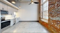 This 470 square foot loft in Pendleton, SC, showcases a perfect blend of industrial charm and modern functionality. The single-floor layout maximizes space efficiency, featuring an open-concept design that seamlessly integrates living areas. Exposed brick walls add character and warmth, contrasting beautifully with the sleek white walls and polished concrete floors. Large, double-hung windows flood the space with natural light and offer scenic views of the surroundings. The kitchen area boasts contemporary white cabinetry and stainless steel appliances, creating a clean, minimalist aesthetic. Overhead, industrial-style lighting and a modern ceiling fan complement the loft's overall design. The bathroom, while not visible in the images, likely continues the modern theme with high-quality fixtures. A notable feature is the high ceilings with exposed ductwork, enhancing the sense of spaciousness. This loft exemplifies urban living, combining historical architectural elements with contemporary comforts in a compact, well-designed space.