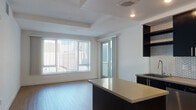 Located at 250 17th St in Oakland, CA, this modern single-floor residence offers a thoughtfully designed layout with contemporary finishes throughout. The open-concept living and kitchen area serves as the heart of the space, featuring warm hardwood-style flooring that extends across the main living zone. The kitchen is well-appointed with dark cabinetry, open shelving, stainless steel appliances including a range, microwave, and refrigerator, and a striking hexagonal tile backsplash. A mobile island with a light countertop provides additional workspace and flexibility. Recessed lighting illuminates the kitchen and living area, complemented by a tray ceiling detail that adds architectural interest. Large windows fitted with vertical blinds allow generous natural light into the living space, which also features access to an outdoor area. The bedroom is carpeted and bright, with a window offering views of the surrounding Oakland cityscape. The bathroom is clean and functional, featuring a full bathtub and shower combination with built-in shelving, hardwood-style flooring, and recessed lighting. The overall aesthetic is modern and understated, with a neutral color palette and clean lines creating a cohesive, move-in-ready environment.