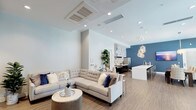 Located at 554 Hawthorne St in Glendale, California, this single-floor community space presents a contemporary, open-plan design that seamlessly integrates multiple functional zones. The interior is finished with warm wood-tone flooring throughout, crisp white walls, and striking deep-blue accent walls that lend a cohesive, modern aesthetic.

The lounge area is anchored by a generously sized sectional sofa and a sculptural round coffee table, all positioned beneath a high ceiling equipped with recessed lighting and a cassette-style HVAC system. Adjacent to the lounge, a media nook features a textured dark-wood backdrop, wall-mounted television, and additional seating, creating an intimate entertainment corner.

The kitchen is a standout feature, outfitted with dark cabinetry, white quartz countertops, and a professional-grade stainless steel range beneath a bold chevron-patterned tile backsplash. A long kitchen island with bar seating bridges the culinary and social spaces, accented by cascading globe pendant lights.

The dining area accommodates multiple seating arrangements and opens directly to an outdoor terrace through floor-to-ceiling glass doors and expansive windows, flooding the space with natural light and offering views of the exterior courtyard. The overall ambiance is polished, welcoming, and well-suited for communal gatherings.