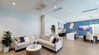 Located at 554 Hawthorne St in Glendale, California, this single-floor community space presents a contemporary, open-plan design that seamlessly integrates multiple functional zones. The interior is finished with warm wood-tone flooring throughout, crisp white walls, and striking deep-blue accent walls that lend a cohesive, modern aesthetic.

The lounge area is anchored by a generously sized sectional sofa and a sculptural round coffee table, all positioned beneath a high ceiling equipped with recessed lighting and a cassette-style HVAC system. Adjacent to the lounge, a media nook features a textured dark-wood backdrop, wall-mounted television, and additional seating, creating an intimate entertainment corner.

The kitchen is a standout feature, outfitted with dark cabinetry, white quartz countertops, and a professional-grade stainless steel range beneath a bold chevron-patterned tile backsplash. A long kitchen island with bar seating bridges the culinary and social spaces, accented by cascading globe pendant lights.

The dining area accommodates multiple seating arrangements and opens directly to an outdoor terrace through floor-to-ceiling glass doors and expansive windows, flooding the space with natural light and offering views of the exterior courtyard. The overall ambiance is polished, welcoming, and well-suited for communal gatherings.
