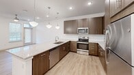 Located at 6930 Prosperity Rd in Huntersville, NC, this one-bedroom, two-bathroom residence offers a well-designed single-floor layout that maximizes its compact footprint. The open-concept kitchen and living area serves as the heart of the space, anchored by a generous granite-topped peninsula illuminated by three pendant lights. The kitchen is equipped with stainless steel appliances—including a range, microwave, and refrigerator—complemented by rich walnut-toned cabinetry, a white subway tile backsplash, and recessed lighting. Light wood-look flooring runs throughout the main living areas, enhancing the bright, airy atmosphere created by multiple windows with blinds.

The bedroom features plush carpeting, a ceiling fan with light fixture, and a window overlooking the outdoors, providing a comfortable retreat. A dedicated closet offers organized storage. The primary bathroom is particularly well-appointed, featuring a dual-sink granite vanity with dark-framed mirrors, modern sconce lighting, a walk-in glass shower, and direct access to a walk-in closet. The secondary bathroom mirrors the same design sensibility with a granite vanity and dark-framed mirror. Clean white walls and consistent modern finishes create a cohesive, contemporary ambiance throughout the residence.