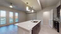 This thoughtfully designed single-floor residence offers a contemporary living experience through a well-planned open layout. The kitchen serves as the heart of the home, showcasing a large center island with a quartz countertop, an undermount stainless steel sink, and elegant pendant lighting overhead. Dark espresso cabinetry extends to the ceiling, providing ample storage, while a mosaic tile backsplash adds visual texture. Full stainless steel appliances, including a French door refrigerator with ice maker, electric range, and built-in microwave, complete the culinary space. Louvered interior doors lend an architectural detail throughout.

The living area flows naturally from the kitchen and features light wood-style flooring, neutral toned walls, and French doors that open to a private balcony, filling the space with natural light and outdoor views. The bedrooms are generously sized, each with the same wood-style flooring, a ceiling fan, and access to natural light through large windows with blinds.

The bathroom is well-appointed with a dark vanity, white quartz countertop, a framed mirror, and a glass-enclosed shower. A dedicated laundry nook with a full-size washer and dryer and an overhead shelf adds everyday convenience to this polished and functional home.