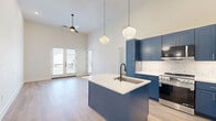 Located at 6758 W Ash St in Frisco, TX, this well-appointed 2-bedroom, 2-bathroom residence offers a thoughtfully designed single-floor layout with a clean, contemporary aesthetic throughout. Light hardwood flooring flows seamlessly across every room, complemented by crisp white walls and tall ceilings that lend an airy, open feel to the space.

The kitchen is a true standout, featuring bold navy blue shaker-style cabinetry that extends floor to ceiling, a white quartz waterfall island with an undermount sink and black matte fixtures, a marble-style tile backsplash, and stainless steel appliances — all illuminated by globe pendant lighting. The adjoining living room benefits from soaring ceilings and a set of French doors alongside an additional exterior door, flooding the space with natural light and providing direct access to a private balcony.

Both bedrooms are generously sized with large windows overlooking the outdoors and dedicated walk-in closets with built-in shelving and hanging rods. The bathrooms are finished with stylish geometric-patterned tile surrounds in a blue and grey palette, white soaking tubs, and sleek matte black fixtures and hardware. Every detail reflects a modern design sensibility, making this a refined and functional Frisco residence.