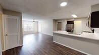 This single-story residence is designed with a practical and cohesive layout that balances open communal spaces with private quarters. The heart of the unit is an open-concept kitchen and living area unified by rich, dark wood-style plank flooring throughout. The kitchen is well-equipped with a full suite of stainless steel appliances, including a refrigerator, range, built-in microwave, and dishwasher. Dark espresso cabinetry pairs with white countertops and a white subway tile backsplash, creating a clean contrast. A peninsula with an integrated sink and extended counter space provides both additional workspace and a natural divide between the kitchen and the living area. The spacious living area benefits from natural light through large windows fitted with blinds, and a ceiling fan adds comfort overhead. Textured ceilings are consistent throughout the unit. The bedroom features plush carpeting, a ceiling fan with a window for natural light, and access to a closet. The bathroom includes a white single-basin vanity with dark wood cabinetry, a large mirror, and a full tub-shower combination with white tile surround and brushed nickel fixtures.