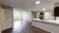 This single-story residence is designed with a practical and cohesive layout that balances open communal spaces with private quarters. The heart of the unit is an open-concept kitchen and living area unified by rich, dark wood-style plank flooring throughout. The kitchen is well-equipped with a full suite of stainless steel appliances, including a refrigerator, range, built-in microwave, and dishwasher. Dark espresso cabinetry pairs with white countertops and a white subway tile backsplash, creating a clean contrast. A peninsula with an integrated sink and extended counter space provides both additional workspace and a natural divide between the kitchen and the living area. The spacious living area benefits from natural light through large windows fitted with blinds, and a ceiling fan adds comfort overhead. Textured ceilings are consistent throughout the unit. The bedroom features plush carpeting, a ceiling fan with a window for natural light, and access to a closet. The bathroom includes a white single-basin vanity with dark wood cabinetry, a large mirror, and a full tub-shower combination with white tile surround and brushed nickel fixtures.