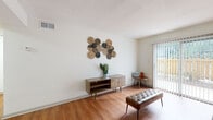 This single-floor residence offers a thoughtfully designed layout that balances comfort and functionality. The living area is a welcoming space anchored by warm hardwood-style flooring, crisp white walls, and a textured ceiling. A large sliding glass door with vertical blinds floods the room with natural light and provides access to an outdoor patio area, framing views of a lush, fenced yard. Mid-century modern furnishings and woven wall art lend the space a stylish, curated character.

The kitchen is efficiently laid out with gray cabinetry, white quartz-style countertops, and a classic white subway tile backsplash. Ample cabinet and counter space make it a practical area for everyday cooking, and hardwood-style flooring continues the cohesive look throughout.

The bedroom is a serene retreat featuring plush carpeting, neutral walls, and a ceiling fan for year-round comfort. A well-sized window allows for natural light while maintaining privacy. The room offers generous open floor space and connects conveniently to adjacent areas of the unit.

The bathroom is clean and functional, featuring a combined tub and shower, a single vanity with a large mirror, and dark marble-style tile flooring that adds a bold contrast to the light walls. Overall, the space presents a cohesive, modern aesthetic with practical finishes throughout.