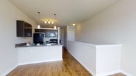 This studio presents a thoughtfully designed single-floor layout that maximizes functionality and style. The open-concept floor plan seamlessly integrates the living and kitchen areas, creating a spacious and airy feel throughout. The kitchen is a standout feature, equipped with dark cabinetry, black appliances including a refrigerator, stove, and microwave, and a granite-topped peninsula that doubles as a breakfast bar. Pendant lighting hangs above the peninsula, adding both task illumination and a modern aesthetic touch. Warm-toned hardwood flooring runs throughout the main living area, lending a welcoming and cohesive look to the space. A half-wall with white trim elegantly defines the living zone while maintaining the open sightlines that make the studio feel larger. Neutral-toned walls provide a versatile backdrop, complemented by white trim and millwork for a clean, polished finish. Recessed and flush-mount ceiling fixtures ensure consistent lighting throughout. The space also includes interior doors leading to additional areas, offering practical storage and utility options. Overall, the studio combines contemporary finishes with a smart, efficient layout ideal for comfortable everyday living.