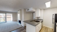 Located at 2235 W Broadway in Anaheim, California, this single-floor unit offers a clean, neutral aesthetic with a practical and open layout. The living room serves as the heart of the space, highlighted by a striking floor-to-ceiling white-paneled fireplace that anchors the room. Plush carpet covers the living area, while wood-look flooring flows through the kitchen and dining spaces. A sliding glass door opens to a private balcony, allowing natural light to fill the room. The kitchen features white cabinetry, gray laminate countertops, and a peninsula with an integrated sink and dishwasher, creating a seamless connection to the living and dining areas. A modest chandelier adds a touch of elegance to the dining space. The bathroom is well-appointed with a gray countertop vanity, an undermount sink, a large mirror, and a separate tub and shower combination. A walk-in closet provides generous storage. Throughout the unit, textured ceilings, neutral wall tones, and consistent finishes contribute to a cohesive and move-in-ready environment. The overall layout is efficient, making excellent use of the available space while maintaining an open and airy feel.