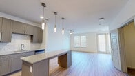 This single-floor residence offers a thoughtfully designed layout encompassing a bedroom, bathroom, den, closet, and dedicated laundry area. The open-concept kitchen and living room serve as the heart of the home, featuring light wood-tone flooring, a ceiling fan, and multiple windows with slatted blinds that invite generous natural light. A sliding glass door provides outdoor access, enhancing the airy feel of the living space.

The kitchen is outfitted with gray flat-front cabinetry, a white subway tile backsplash, granite countertops, and a full suite of stainless steel appliances including a refrigerator with ice maker, range, microwave, and dishwasher. A peninsular island with matching granite and pendant lighting above adds both prep space and a casual dining option.

The bedroom features plush carpeting, a ceiling fan, and dual windows offering natural light and outdoor views. The bathroom connects to a dedicated walk-in closet and includes a granite-topped vanity with gray cabinetry, a glass-enclosed shower, and wood-look flooring. The den provides a versatile additional space with the same light hardwood flooring found throughout the main living areas. An in-unit laundry area completes the functional layout of this modern, move-in-ready residence.