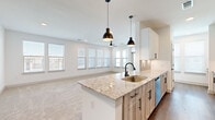 This well-appointed single-floor residence offers a thoughtfully designed layout across two bedrooms, two bathrooms, and a combined kitchen and living area. The open-concept main living space serves as the centerpiece of the home, where the kitchen features a large island topped with granite countertops, a undermount sink with matte black fixtures, and stainless steel appliances including a refrigerator, microwave, and range. White upper cabinetry contrasts with warm wood-toned lower cabinets, while two black industrial-style pendant lights hang above the island. The living area extends from the kitchen, bathed in natural light from multiple windows fitted with blinds.

Both bedrooms are carpeted and generously sized, each with ceiling fans and large windows offering outdoor views. The primary bedroom connects to a well-equipped en-suite bathroom featuring a double vanity with granite countertops, wood-toned cabinetry, matte black fixtures, and backlit mirrors. A walk-in closet with built-in shelving and dual hanging rods provides substantial storage. The second bedroom is equally bright and versatile. Hardwood-style flooring flows through the kitchen, hallway, and bathrooms, while a dedicated entrance provides a welcoming transition into the home.