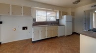 This single-floor home offers a straightforward, functional layout spread across several well-defined spaces. The kitchen is designed in a galley style, featuring white cabinetry, dark laminate countertops, and tile-pattern vinyl flooring. It is equipped with a gas range, dishwasher, refrigerator, and a double stainless steel sink positioned beneath a window that allows natural light into the space. A secondary exterior door provides convenient access from the kitchen area.

The living areas are finished with neutral-toned carpet and ceiling fans, contributing to a comfortable, practical atmosphere. A sliding glass door in one of the main living spaces connects the interior to the outdoors, while additional windows allow natural light to filter throughout. The bedrooms are also carpeted, bright, and modestly sized, each benefiting from natural light provided by blinds-fitted windows.

The bathroom is clean and simply appointed, featuring a vanity with a dark wood cabinet base, a wall-mounted mirror, a toilet, and a bathtub with a shower. Tile-pattern vinyl flooring carries through from the kitchen into this space, maintaining visual consistency. Overall, the home presents a clean, neutral interior ready for personalization.