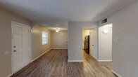 This single-floor residence offers a functional and cohesive layout designed for comfortable everyday living. The main living area is generously sized, featuring durable wood-look plank flooring, neutral warm-toned walls, a textured ceiling, and a large window with vertical blinds that invites natural light and offers views of the surrounding greenery. A secure entry door with a window panel leads into the space, creating a welcoming entryway.

The living area flows seamlessly through an arched opening into a dedicated dining area, accented by a ceiling fan with a light fixture. This connected layout supports an easy transition between gathering and dining spaces. The galley-style kitchen runs along both sides with ample granite-look countertops, white cabinetry, and stainless steel appliances, including a refrigerator, maximizing storage and workspace efficiency.

The bedrooms are well-proportioned, each featuring wood-look flooring, ceiling fans, natural light from windows, and louvered closet doors providing practical storage. The bathroom is neatly appointed with white cabinetry, a granite-look vanity countertop, a toilet, and a tub-shower combination with a window for ventilation. Consistent flooring and a neutral color palette throughout the unit create a clean, unified aesthetic.