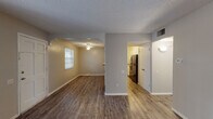 This single-floor residence offers a functional and cohesive layout designed for comfortable everyday living. The main living area is generously sized, featuring durable wood-look plank flooring, neutral warm-toned walls, a textured ceiling, and a large window with vertical blinds that invites natural light and offers views of the surrounding greenery. A secure entry door with a window panel leads into the space, creating a welcoming entryway.

The living area flows seamlessly through an arched opening into a dedicated dining area, accented by a ceiling fan with a light fixture. This connected layout supports an easy transition between gathering and dining spaces. The galley-style kitchen runs along both sides with ample granite-look countertops, white cabinetry, and stainless steel appliances, including a refrigerator, maximizing storage and workspace efficiency.

The bedrooms are well-proportioned, each featuring wood-look flooring, ceiling fans, natural light from windows, and louvered closet doors providing practical storage. The bathroom is neatly appointed with white cabinetry, a granite-look vanity countertop, a toilet, and a tub-shower combination with a window for ventilation. Consistent flooring and a neutral color palette throughout the unit create a clean, unified aesthetic.