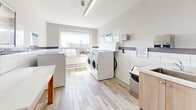 Located at 7 Elizabeth St N in Mississauga, Ontario, this shared laundry facility is a clean, efficiently designed space that provides residents with all the essentials for convenient in-building laundry access. The room features light wood-look flooring and white subway tile wainscoting accented by a horizontal band of dark tile, giving the space a crisp, contemporary aesthetic that is easy to maintain.

Multiple commercial-grade front-loading and top-loading washing machines and dryers are arranged along the walls, offering ample capacity for resident use. A utility sink with a wood-toned cabinet base is positioned along one wall, providing a practical handwashing or pre-treatment station. A sturdy wooden folding table occupies the center of the room, offering a convenient surface for sorting and folding laundry.

A large window along one wall fills the space with natural light and provides views of the surrounding neighbourhood, creating a bright and pleasant environment. Posted operating instructions and service information are clearly displayed on the walls for easy reference. Fluorescent overhead lighting ensures the room remains well-lit at all times. The layout is thoughtfully organized to allow comfortable movement throughout the space, making this laundry room a practical and functional amenity for residents of the building.