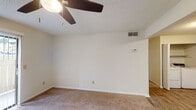 This single-floor residence offers a functional and comfortable layout across several distinct living areas. The kitchen stands out with its rich, dark cabinetry providing generous storage, light-toned countertops, and wood-look plank flooring. Black appliances, including a range, refrigerator, and dishwasher, complement the cabinetry, and a stainless steel sink completes the space. The layout flows efficiently, making the kitchen practical for everyday use.

The living areas are finished with wall-to-wall carpeting in a neutral tone, creating a warm and cohesive atmosphere throughout. Ceiling fans with integrated lighting fixtures are present in the main living spaces, supporting air circulation and ambient lighting. A sliding glass door fitted with vertical blinds allows natural light to pour in and provides access to an outdoor area. Additional rooms feature windows with blinds, further enhancing natural light throughout the unit.

The bathroom includes a full-size soaking tub with a shower, finished with clean white surround panels and chrome fixtures. Textured ceilings are consistent throughout the unit. The overall design is straightforward and neutral, offering a versatile canvas suitable for a variety of living arrangements.
