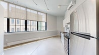 Located at 1 Upper Falls Rd in Biddeford, Maine, this thoughtfully designed unit showcases a clean industrial aesthetic with modern upgrades. Polished concrete floors run throughout the single-floor layout, complementing the soaring ceilings and exposed structural elements that reflect the building's industrial heritage.

The kitchen is a standout feature, outfitted with white shaker-style cabinetry, dark granite countertops, a classic subway tile backsplash, and a full suite of stainless steel appliances including a range, dishwasher, and refrigerator. A wall-mounted split HVAC unit ensures year-round climate control.

Large, multi-pane factory-style windows flood the main living area with abundant natural light, offering views of the surrounding Biddeford neighborhood. Roller shades provide privacy and light control. A baseboard heater runs beneath the windows, adding to the space's functional design.

The bathroom is finished with white shaker vanity cabinetry, a light stone countertop, brushed nickel fixtures, a large mirror, and a walk-in shower. Two closets provide practical storage solutions. A hallway connects the space efficiently. The minimalist, neutral color palette of soft grays and whites throughout creates a bright, cohesive ambiance well-suited for modern living.