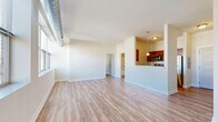 Located at 901 Draper Ave. in Schenectady, NY, this 1-bedroom, 1-bathroom residence offers a thoughtfully designed single-floor layout that maximizes functionality and comfort. The combined kitchen and living area forms the heart of the home, where the kitchen features rich, dark wood cabinetry, granite-style countertops, stainless steel appliances including a full-size refrigerator and dishwasher, and a pendant light fixture above the pass-through opening. The living area is filled with natural light from a wide bank of windows overlooking the surrounding neighborhood, and is finished with durable wood-look flooring that extends throughout the main living spaces. The bedroom is a comfortable retreat with soft carpeting, a window with outdoor views, and direct access to a generously sized walk-in closet outfitted with wire shelving and hanging rods. The bathroom includes a full tub-shower combination with chrome fixtures and tiled flooring. Exposed ductwork running along the upper walls adds an urban, industrial character to the space. Clean white walls and an abundance of windows create a bright, airy ambiance throughout this well-organized residence.