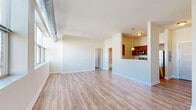 Located at 901 Draper Ave. in Schenectady, NY, this 1-bedroom, 1-bathroom residence offers a thoughtfully designed single-floor layout that maximizes functionality and comfort. The combined kitchen and living area forms the heart of the home, where the kitchen features rich, dark wood cabinetry, granite-style countertops, stainless steel appliances including a full-size refrigerator and dishwasher, and a pendant light fixture above the pass-through opening. The living area is filled with natural light from a wide bank of windows overlooking the surrounding neighborhood, and is finished with durable wood-look flooring that extends throughout the main living spaces. The bedroom is a comfortable retreat with soft carpeting, a window with outdoor views, and direct access to a generously sized walk-in closet outfitted with wire shelving and hanging rods. The bathroom includes a full tub-shower combination with chrome fixtures and tiled flooring. Exposed ductwork running along the upper walls adds an urban, industrial character to the space. Clean white walls and an abundance of windows create a bright, airy ambiance throughout this well-organized residence.