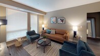 This well-appointed single-floor residence offers a thoughtfully designed layout with a cohesive contemporary aesthetic. The kitchen is a functional centerpiece, featuring taupe flat-front cabinetry, granite countertops, a white subway tile backsplash, stainless steel appliances including a gas range and full-size refrigerator, and a central island with pendant lighting and bar seating. Wood-look flooring extends through the kitchen and connects seamlessly to the living area, where large windows with blinds admit generous natural light and provide access to an exterior door. The living space is comfortably proportioned and finished with warm neutral wall tones. Two bedrooms feature plush carpet, natural light from windows, and access to closet storage, including a walk-in closet equipped with multi-tier wire shelving. The primary bathroom includes a glass-enclosed walk-in shower, a vanity, and tile flooring, with a direct connection to the bedroom. A second full bathroom offers a tub-shower combination and large-format tile flooring. Throughout the unit, a consistent warm greige palette, clean trim details, and modern hardware contribute to a polished, move-in-ready atmosphere.