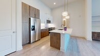 Located at 2124 American Industrial Way in Chamblee, GA, this thoughtfully designed one-bedroom unit offers a bright, contemporary living experience across a single floor. The open layout is anchored by impressive ceiling heights and an abundance of natural light streaming through dramatic floor-to-ceiling windows fitted with sleek black frames, offering views of the surrounding exterior landscape.

The kitchen is a standout feature, showcasing a two-tone design with rich wood-grain lower cabinetry paired with crisp white upper cabinets and a geometric tile backsplash. A central island with a white quartz countertop, undermount sink, and gold-toned faucet serves as both a functional workspace and a gathering point. Stainless steel appliances, including a French door refrigerator, range, and microwave, complete the modern aesthetic. Light wood-look flooring runs throughout the main living and kitchen areas, adding warmth to the neutral palette.

The generously sized primary bedroom is finished with plush carpeting, a ceiling fan, and access to a dedicated walk-in closet equipped with wire shelving for organized storage. The bedroom also benefits from natural light through large windows. The living area features built-in shelving, offering functional display and storage options. Overall, the space conveys a clean, modern ambiance with high-quality finishes throughout.