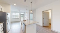 Located at 11750 Alliance Cir in Chester, VA, this well-appointed one-bedroom, one-bathroom unit offers a thoughtfully designed open-concept floor plan with contemporary finishes. The kitchen serves as the focal point of the main living area, featuring a central island with a granite countertop and undermount sink, elegant pendant lighting, white shaker-style cabinetry with black hardware, a gray tile backsplash, and a full suite of stainless steel appliances including a range, over-the-range microwave, dishwasher, and refrigerator. Light wood-look flooring flows throughout the main living areas, complementing the bright, neutral color palette. Large windows in the living area allow ample natural light to fill the space, and a ceiling fan adds comfort. The bedroom is carpeted and generously sized, with a ceiling fan and a window offering outdoor views. A hallway leads to the full bathroom, which includes a tub and shower combination with chrome fixtures, and connects to a dedicated closet for additional storage. The unit also features multiple interior doors providing privacy and organization. The clean, modern aesthetic and efficient layout make this a highly functional and attractive living space.