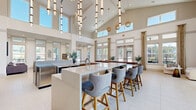Located in Port Wentworth, Georgia, this single-floor clubhouse offers a generously sized, thoughtfully designed communal space that blends sophisticated aesthetics with practical functionality. The architecture is defined by dramatically vaulted ceilings that rise well above typical height, lined with clerestory windows that flood the interior with natural light throughout the day.

The main gathering area anchors the space with a large kitchen island topped in sleek quartz, surrounded by upholstered bar seating with nailhead-trim detailing. Warm wood cabinetry, stainless steel appliances, and pendant lighting contribute to a refined yet welcoming atmosphere. A long built-in window bench runs along an expansive wall of floor-to-ceiling windows, offering outdoor views of the surrounding community.

A lounge area features a geometric tile accent wall with an inset display screen, complemented by plush sectional seating and curated artwork. An additional seating nook with large windows provides a bright, airy retreat furnished with contemporary accent chairs and tile flooring.

A dedicated conference room provides a more intimate setting, highlighted by a textured teal accent wall, light wood plank wall cladding, a natural wood table, and sculptural pendant lighting. Throughout, light-toned flooring, neutral walls, and carefully selected furnishings create a cohesive, upscale ambiance.