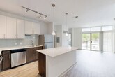 Located at 299 N Highland Ave in Atlanta's dynamic Old Fourth Ward, this modern 2-bedroom, 1-bathroom residence offers a thoughtfully designed open-concept layout with contemporary finishes throughout. The combined kitchen and living area serves as the heart of the home, anchored by a sleek central island with crisp white quartz countertops. The kitchen is well-appointed with stainless steel appliances, two-tone cabinetry featuring white upper cabinets and dark lower cabinets, a light gray subway tile backsplash, and track lighting complemented by elegant pendant lights. Light wood-style flooring runs through the main living areas, adding warmth to the modern aesthetic. Large floor-to-ceiling windows and a glass-door balcony access flood the living room with natural light and provide outdoor views. The primary bedroom offers a comfortable retreat with plush carpeting, a ceiling fan, and direct access to a dedicated closet and the full bathroom. The bathroom features large-format tile flooring, a dark wood vanity with a white countertop, and a spacious walk-in glass shower. The second bedroom also features light hardwood-style flooring and bright white walls. Two closets provide ample storage throughout the residence.