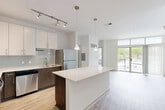 Located at 299 N Highland Ave in Atlanta's dynamic Old Fourth Ward, this modern 2-bedroom, 1-bathroom residence offers a thoughtfully designed open-concept layout with contemporary finishes throughout. The combined kitchen and living area serves as the heart of the home, anchored by a sleek central island with crisp white quartz countertops. The kitchen is well-appointed with stainless steel appliances, two-tone cabinetry featuring white upper cabinets and dark lower cabinets, a light gray subway tile backsplash, and track lighting complemented by elegant pendant lights. Light wood-style flooring runs through the main living areas, adding warmth to the modern aesthetic. Large floor-to-ceiling windows and a glass-door balcony access flood the living room with natural light and provide outdoor views. The primary bedroom offers a comfortable retreat with plush carpeting, a ceiling fan, and direct access to a dedicated closet and the full bathroom. The bathroom features large-format tile flooring, a dark wood vanity with a white countertop, and a spacious walk-in glass shower. The second bedroom also features light hardwood-style flooring and bright white walls. Two closets provide ample storage throughout the residence.