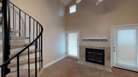 This two-story, 2-bedroom, 2-bathroom residence with a loft offers a well-designed layout across a comfortable footprint. The living room serves as the architectural centerpiece, boasting dramatic vaulted ceilings that soar upward and are illuminated by strategically placed upper windows, flooding the space with natural light. A tile-surround fireplace with a white mantel shelf anchors the room, while a ceiling fan with integrated lighting adds functionality. A curved staircase with a sleek black railing adds a refined design element and leads to the upper loft level, which overlooks the main living area below.

The kitchen features white cabinetry, light countertops, and black appliances, including an electric range and over-the-range microwave, complemented by dark hardwood-style flooring. Both bathrooms are finished with white vanities, lighted mirrors, and tub-shower combinations. The bedrooms offer carpeted floors and vaulted or angled ceilings, contributing to an airy feel throughout. One bedroom features a recessed window nook that adds architectural character. Neutral warm tones throughout the home create a cohesive and inviting atmosphere well-suited for a variety of furnishing styles.