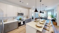 Located at 1803 S 46th Street in Rogers, Arkansas, this well-appointed two-bedroom, two-bathroom residence offers a thoughtfully designed single-level layout. The open-concept kitchen serves as the heart of the home, showcasing two-tone cabinetry with white upper and gray lower cabinets, a subway tile backsplash, stainless steel appliances, and a spacious waterfall-edge island with an integrated sink and seating — ideal for dining and entertaining. Pendant lighting adds a modern touch above the island. Light wood-style flooring flows throughout the main living areas, complementing the bright, neutral color palette. The generously sized primary bedroom features a ceiling fan and direct access to a private en-suite bathroom with a dual-sink vanity, gray cabinetry, and white quartz countertops. The second bedroom is bright and comfortable, benefiting from large windows that invite natural light and offer views of the surrounding community. Both bedrooms are served by dedicated closets with wire shelving systems for organized storage. A private balcony extends the living space outdoors, offering open views of the developing Rogers skyline and surrounding landscape. Clean architectural lines, recessed lighting, and modern fixtures are consistent throughout, creating a cohesive and contemporary living environment.