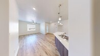 Unit B23 at 185 S Colvin St in Colorado City, Arizona is a thoughtfully designed single-floor residence offering four bedrooms and two full bathrooms. The open-concept kitchen and living area serves as the heart of the home, featuring light wood-look flooring that extends throughout the common spaces, a ceiling fan, and a window that brings in natural light. The kitchen is outfitted with wood-grain cabinetry in a contemporary finish, clean white countertops, pendant lighting over the sink, and a stainless steel dishwasher. A dedicated pantry provides additional storage. The four bedrooms are carpeted for comfort, with clean white walls and windows in select rooms. One bedroom includes a closet. The two bathrooms share a consistent design aesthetic, each featuring a tiled shower-tub combination with brushed gold or brushed nickel fixtures, wood-grain vanity cabinetry, and wood-look flooring. A dedicated laundry room with washer hookups and shelving adds everyday convenience. Two hallways connect the rooms efficiently. The overall ambiance is clean, modern, and neutral throughout.