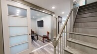 This multi-level residence spans three floors, offering a practical and well-designed layout across two bedrooms and two bathrooms. Light gray hardwood-style flooring flows consistently throughout the home, lending a cohesive and contemporary feel to each level. Four staircases connect the floors, ensuring efficient circulation throughout the space.

The kitchen is a standout feature, equipped with stainless steel appliances including a range, microwave, and dishwasher. Dark espresso cabinetry is complemented by granite countertops and a mosaic tile backsplash, while recessed lighting and a natural-light-admitting exterior door enhance the room's bright, functional atmosphere.

The living room features a wall-mounted flat-screen TV, recessed lighting, and light-toned walls, creating a clean and relaxed gathering space. Sliding glass-panel doors connect it to the hallway, adding an open, airy quality.

Both bathrooms are finished with large-format marble-style tile. One includes a glass-enclosed walk-in shower with a wood-toned vanity, while the second offers a soaking tub with a window overlooking greenery, accented by decorative mosaic tile borders.

The bedrooms are bright and neutral, each featuring closets and windows, with the spacious primary bedroom offering ample room for furnishings.