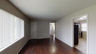 This single-floor residence offers a clean, functional layout with a consistent design aesthetic throughout. Rich, dark hardwood flooring runs through the living areas and bedrooms, providing warmth and character to each room. The living spaces are generously sized, featuring neutral gray walls and large windows dressed with vertical blinds that allow abundant natural light to fill the interior.

The kitchen is thoughtfully appointed with dark espresso cabinetry, granite-style countertops, and a tile backsplash featuring a decorative diamond pattern. Stainless steel appliances — including an electric range, dishwasher, and refrigerator — are complemented by light tile flooring, creating a practical and visually cohesive cooking space. A door in the kitchen provides convenient exterior access.

The bedrooms are well-proportioned, each benefiting from multiple windows with horizontal blinds that frame views of the surrounding outdoors, ensuring bright and airy environments. The bathroom is finished with large-format wall tiles surrounding a full bathtub and shower combination, a white vanity with an integrated sink, and a mirrored medicine cabinet. Natural light enters through a window above the tub, enhancing the room's fresh, clean atmosphere. Overall, the space presents a straightforward and practical living environment with consistent finishes throughout.