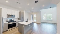Located at 900 N Allen Ave in Richmond, VA, this well-appointed two-story unit offers 3 bedrooms and 5 bathrooms across two thoughtfully designed floors. The main level opens into a bright, open-concept kitchen and living area. The kitchen is outfitted with two-tone cabinetry — crisp white upper cabinets paired with gray lower cabinets — stainless steel appliances including a range, microwave, and refrigerator, and a large center island with a undermount sink and white quartz countertops. Warm hardwood-style flooring and recessed lighting complete the space. The living room is a standout feature, boasting soaring double-height ceilings, oversized windows, and sliding glass doors that flood the room with natural light and offer views of the surrounding neighborhood. The upper level houses the bedrooms, each featuring hardwood-style flooring, ceiling fans, and generous windows with neighborhood views. The primary bedroom is a comfortable retreat with ample proportions. The five bathrooms are finished in a clean, contemporary style with large-format tile flooring, frameless glass-enclosed showers, gray vanities with white countertops, and sleek fixtures throughout. The staircase connects both levels seamlessly, making this a highly functional and modern living space.