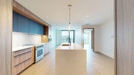 Located in Denver's vibrant South Quebec Street corridor, this thoughtfully designed one-bedroom, one-bathroom residence offers a seamless blend of modern aesthetics and functional living. Light-toned hardwood flooring runs throughout, creating a warm, cohesive foundation that complements the crisp white walls and clean architectural lines.

The open-concept kitchen and living area serves as the heart of the home. The chef's kitchen is outfitted with custom wood cabinetry in a soft natural finish, bold slate-blue upper cabinets, a large waterfall-edge island with an integrated sink, and a sleek linear pendant light overhead. High-end stainless steel appliances complete this sophisticated culinary space.

Floor-to-ceiling windows and a glass-paneled sliding door in the living area flood the space with natural light while framing expansive elevated views of the Denver skyline and surrounding cityscape. A ceiling fan adds both comfort and style to this bright, airy room.

The generously sized primary bedroom features its own private balcony access through a black-framed glass door, offering additional outdoor views. A dedicated closet provides ample storage.

The spa-inspired bathroom is a standout feature, showcasing large-format white marble tile, a freestanding soaking tub within a glass-enclosed wet room, a dual-sink vanity with warm wood cabinetry, matte black fixtures, and elegant gold accent lighting — a refined retreat within this modern Denver residence.