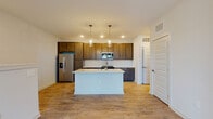 This thoughtfully designed residence spans multiple levels connected by a carpeted staircase with a clean white handrail, offering a comfortable and functional layout. The open-concept kitchen serves as a central highlight, featuring rich dark-stained cabinetry extending to the ceiling for ample storage, white quartz countertops, and a full suite of stainless steel appliances including a side-by-side refrigerator with ice maker, electric range, built-in microwave, and dishwasher. A white subway tile backsplash adds a classic touch, while a central island with pendant lighting overhead provides additional prep space and casual seating. Light hardwood-style flooring runs throughout the main living areas, complementing the bright, neutral color palette. The open living area features recessed lighting, a ceiling fan, and windows that invite natural light. Bedrooms are finished with plush carpet and ceiling fans, offering a cozy retreat. The bathroom is well-equipped with a glass-enclosed walk-in shower, wood-toned vanity cabinetry, and white countertops, all set on matching hardwood-style flooring. Throughout the residence, panel-style doors, crisp white trim, and a consistent modern finish create a cohesive and move-in-ready environment.