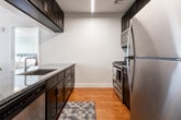Located at 117–125 Bloomfield Ave in Montclair, NJ, this well-designed single-floor residence offers a clean, contemporary aesthetic throughout. The open-plan living and dining area serves as the heart of the unit, featuring warm hardwood flooring, soft neutral walls, and a sliding glass door that allows natural light to fill the space. The kitchen is outfitted with dark espresso cabinetry reaching to the ceiling, stainless steel appliances including a refrigerator and gas range, granite-style countertops, and hardwood floors that extend from the main living area. Two carpeted bedrooms provide comfortable retreats, each with windows allowing natural light and vertical blinds for privacy. The primary bedroom is generously proportioned, offering ample space for furnishings. Both bathrooms are finished with light wood-look tile flooring, dark vanity cabinetry, and gray stone countertops. One bathroom features classic white subway tile surrounding a shower-tub combination, while the second is appointed with a framed mirror and a tub alcove. Throughout the unit, a cohesive palette of white walls, dark wood accents, and neutral flooring creates a modern yet inviting atmosphere well-suited to everyday living in vibrant Montclair.