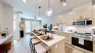 Located at 1445 S Power Rd in Mesa, AZ, this well-appointed one-bedroom, one-bathroom residence offers a thoughtfully designed single-level layout with modern finishes throughout. The open-concept kitchen and living area serves as the heart of the home, featuring light wood cabinetry, a white quartz countertop island with bar seating, stainless steel appliances — including a gas range, microwave, and French door refrigerator — a white subway tile backsplash, and matte black fixtures. Statement glass pendant lights illuminate the island, adding a refined touch. The kitchen flows seamlessly into the living room, which is bathed in natural light from large windows and a glass patio door. Light wood-tone flooring extends throughout the main living areas, creating a warm, cohesive aesthetic. The bedroom offers a comfortable retreat with plush carpet, a ceiling fan, and a generously sized window. The bathroom features a wood-tone vanity with white countertop, matte black hardware, and a glass-enclosed shower. A dedicated laundry area with stacked full-size washer and dryer adds everyday convenience. Clean white walls and abundant natural light give the entire residence a bright, contemporary ambiance.